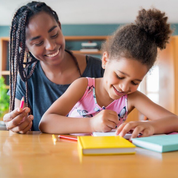 women and girl sitting at desk working together writing in notebook