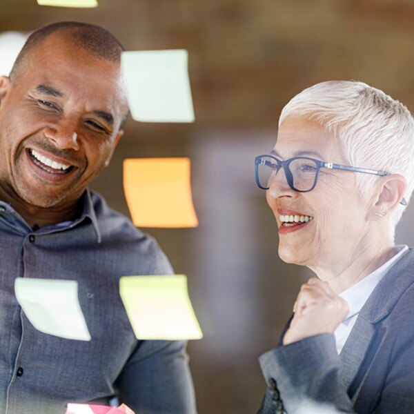 two coworkers looking at board smiling reading sticky notes