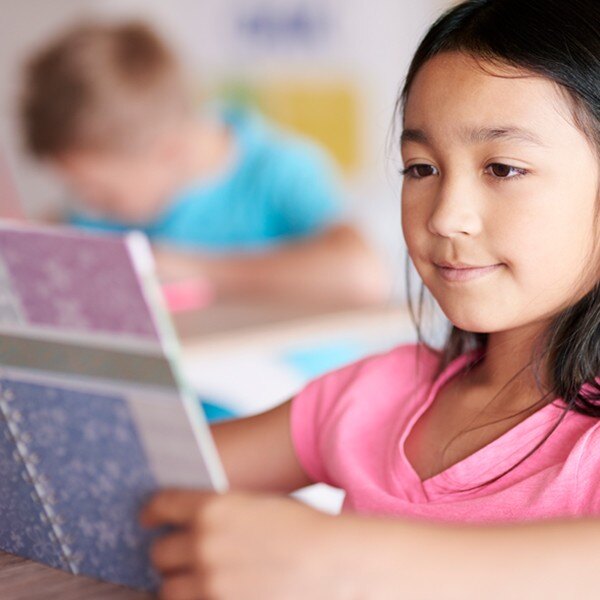 student sitting at desk in classroom reading book