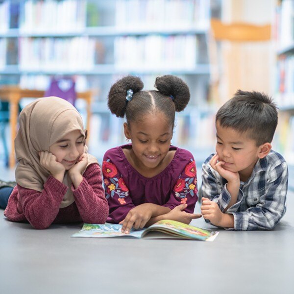 three children lying on the floor reading a book in the library