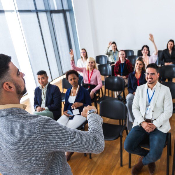 man speaking to group of individuals sitting in chairs 