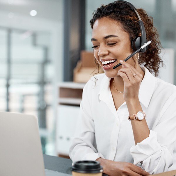 female worker sitting at desk in office looking at laptop talking into headset