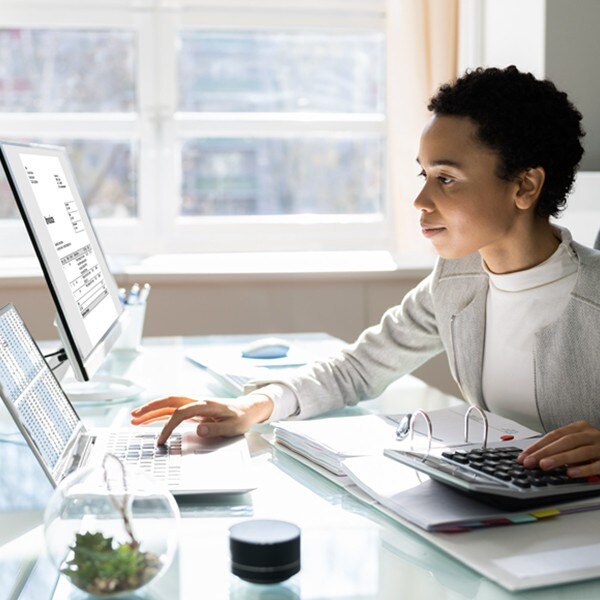 female worker sitting at desk looking at laptop and using calculator