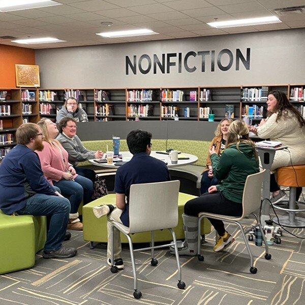 eight individuals sitting around table in library talking and working with each other