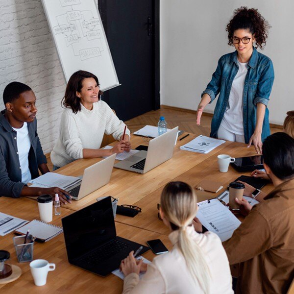 seven coworkers sitting in conference room in a meeting working together laptops notebooks