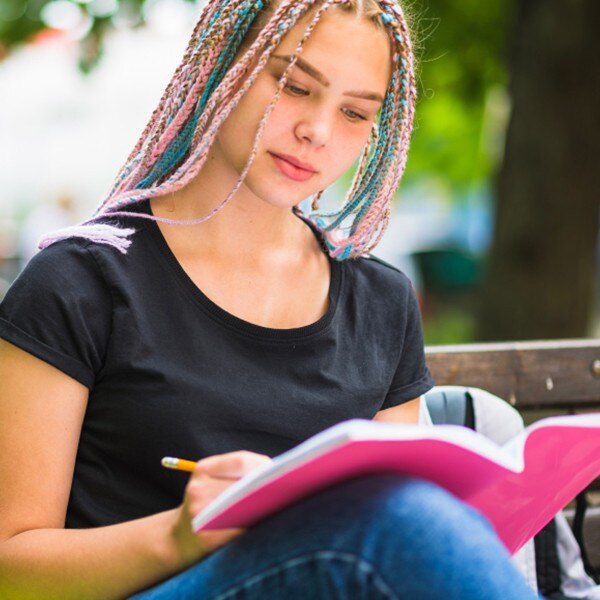 student sitting outside on bench reading and writing in book