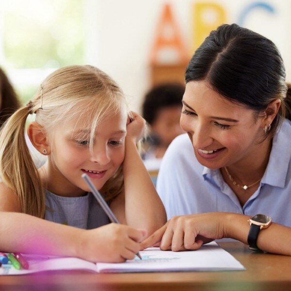 teacher helping student sitting at desk with homework