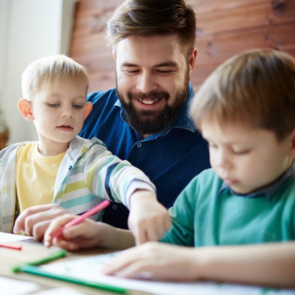 two young boys and man sitting at desk working together coloring notebook