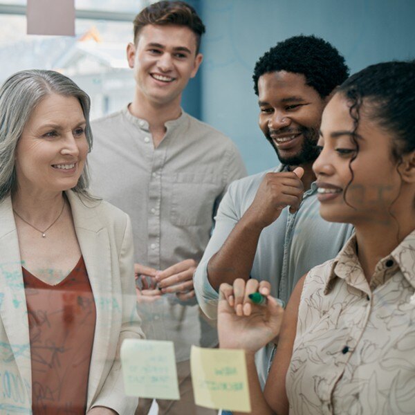 four coworkers standing next to each other looking and writing on board