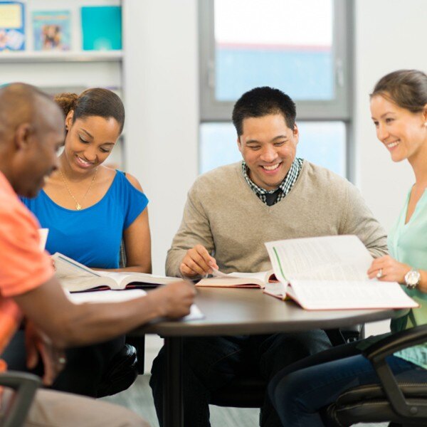 four coworkers sitting around table working together smiling reading books