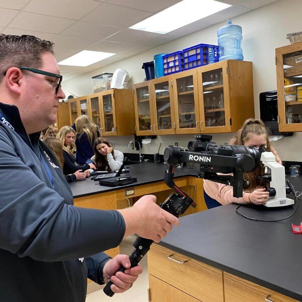 man taking a video of student working with a microscope in a science lab class