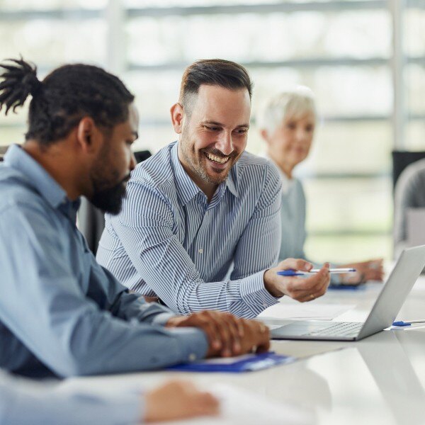 coworkers sitting at desk in conference room working together looking at laptop