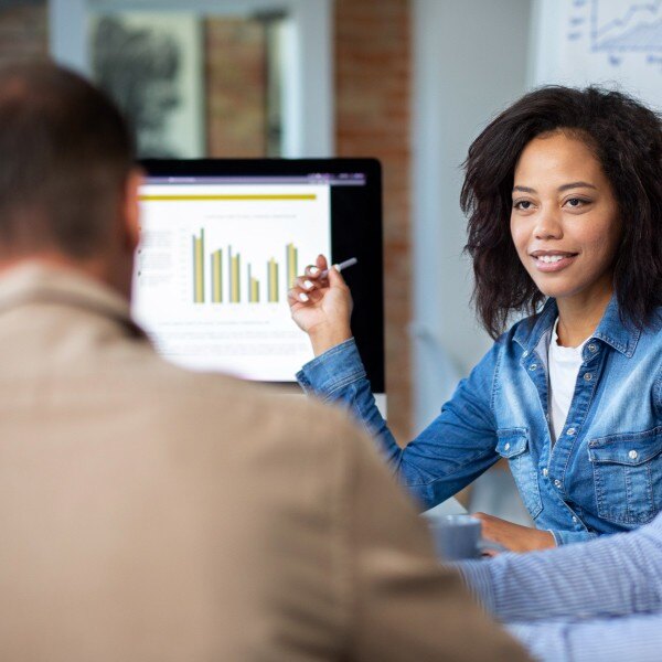 three coworkers sitting around table in conference room looking at computer screen data charts